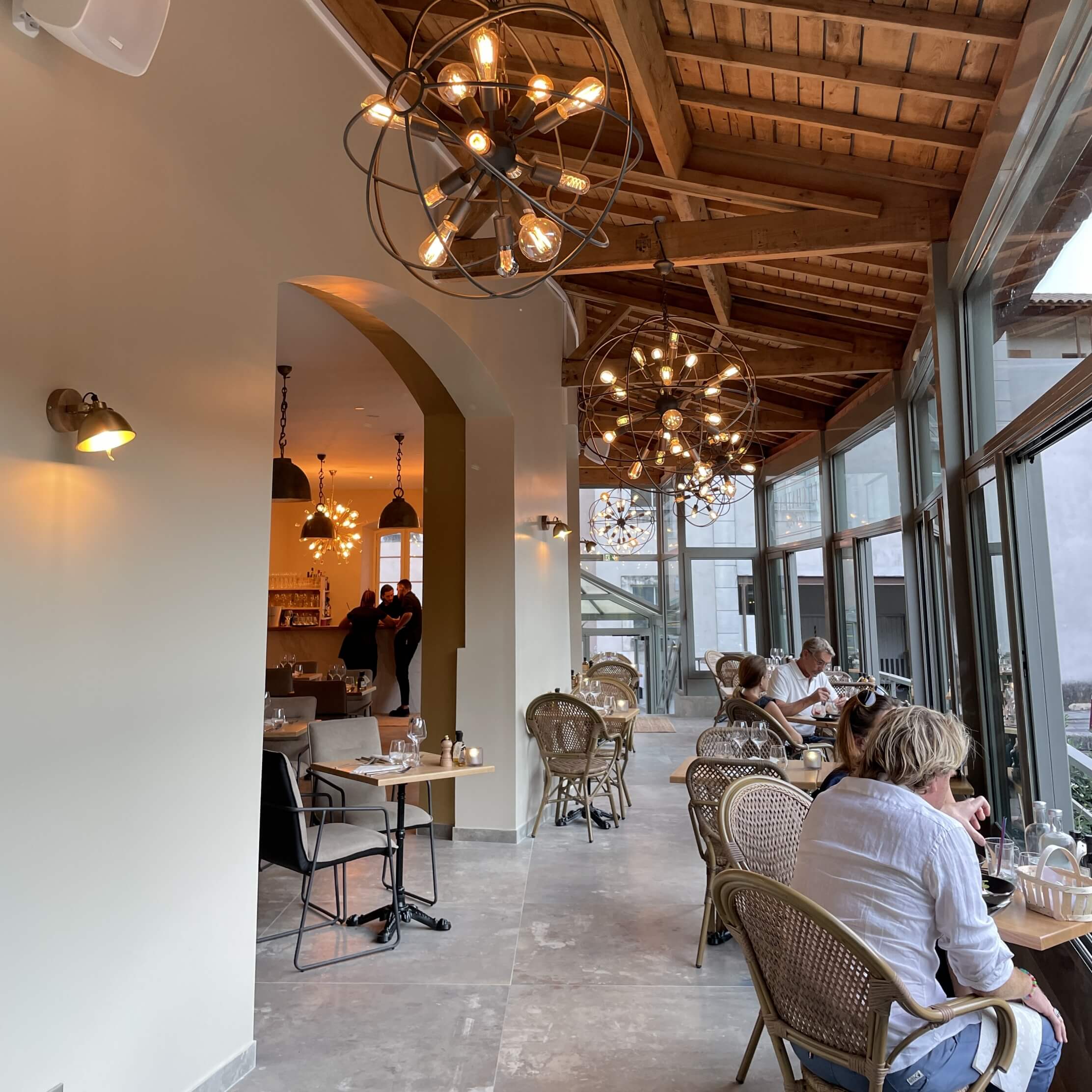tables installées le long de la verranda, face à la Sorgue, des lustres de style industriels sont installés aux charpentes