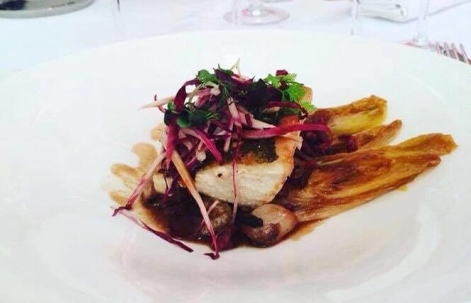 assiette de poisson recouvert de petits légumes et sauce brune
