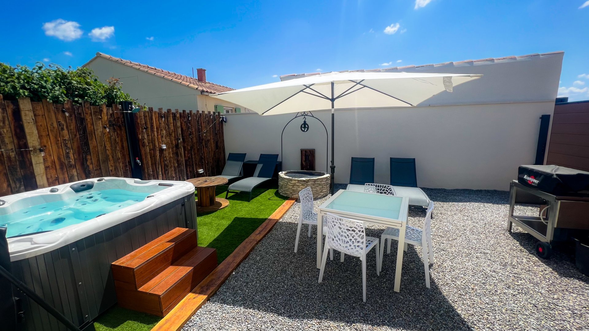     Requête réussie  Une petite terrasse extérieure avec un bain à remous en bois sombre sur la gauche et un ensemble de chaises et table blanches sur la droite, le tout sur un sol en gravier. Un grand parasol blanc ouvert est visible en arrière-plan.