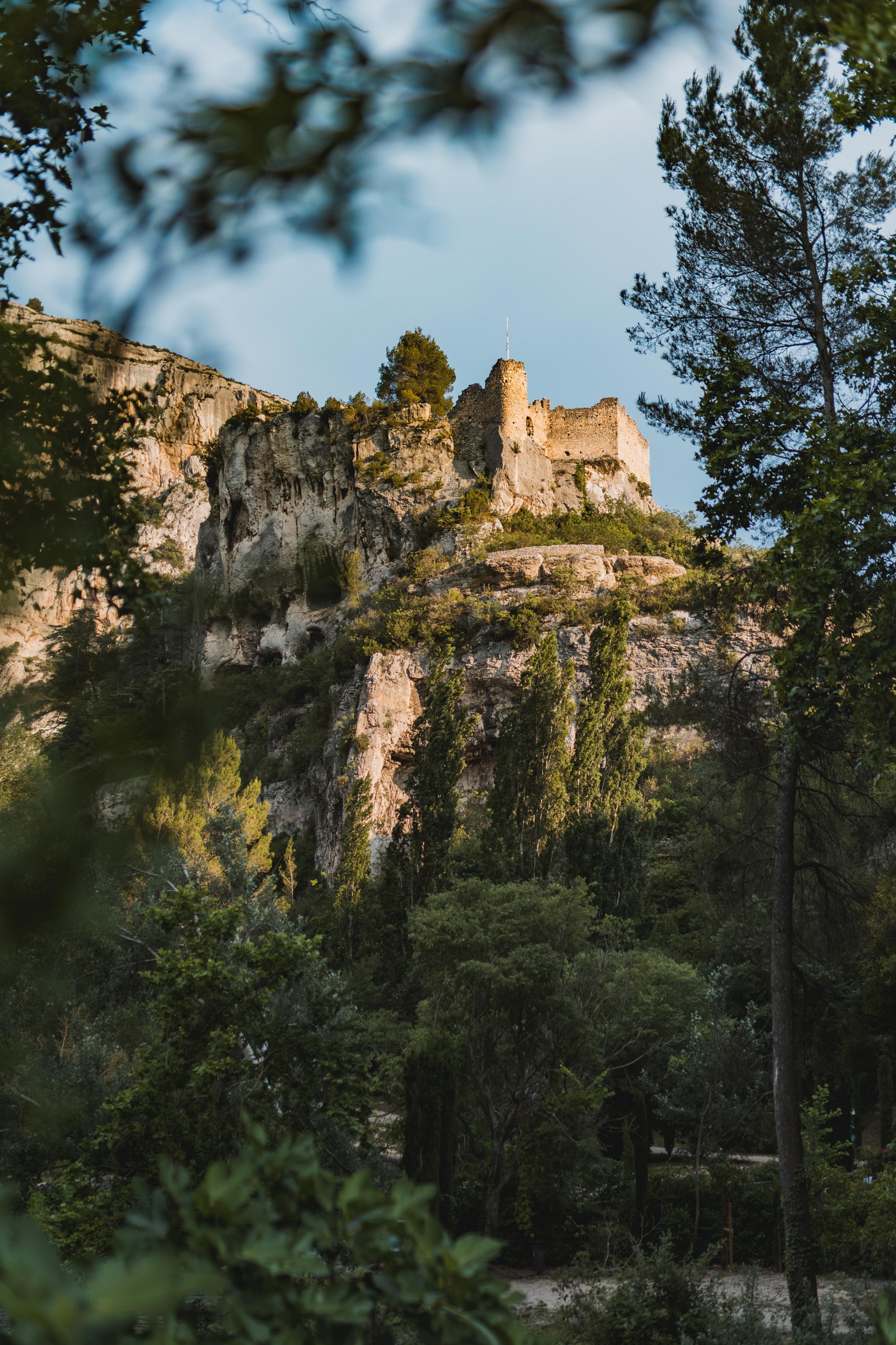 Les ruines du Château de Philippe de Cabassolle se dressant au sommet d'une falaise rocheuse, entourées d'une forêt verdoyante sous un ciel clair à Fontaine-de-Vaucluse.