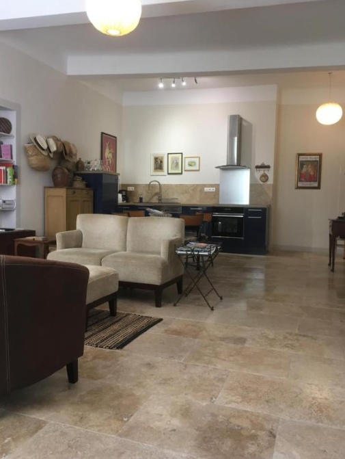 Un espace de vie ouvert avec un salon cosy doté de canapés en tissu clair et cuir foncé, et une cuisine moderne bleu marine avec un évier et une hotte. Le sol est carrelé, et des œuvres d'art sont accrochées aux murs.