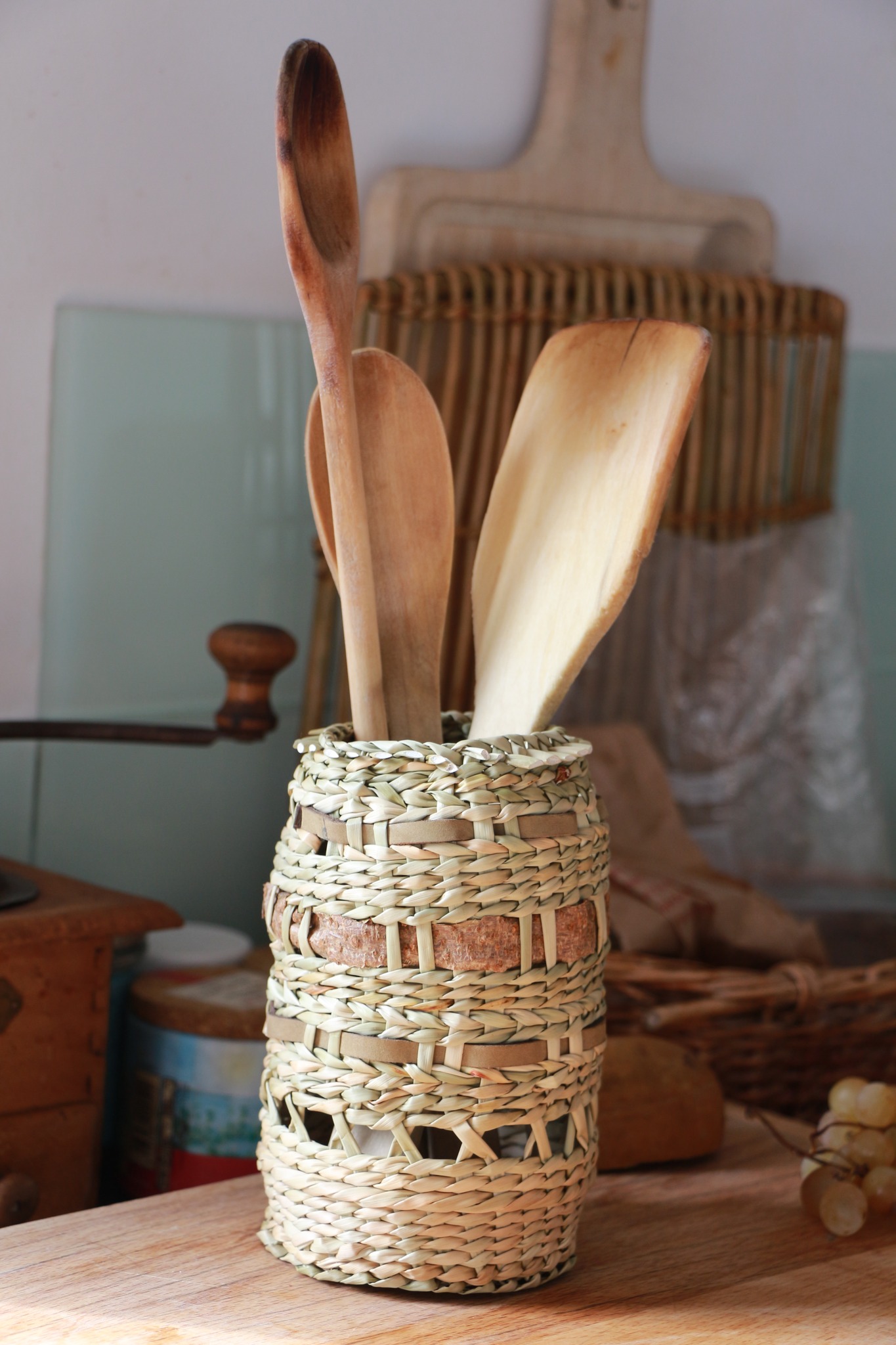 Un porte-ustensiles tressé en paille, contenant des cuillères et des spatules en bois, posé sur une surface en bois clair.