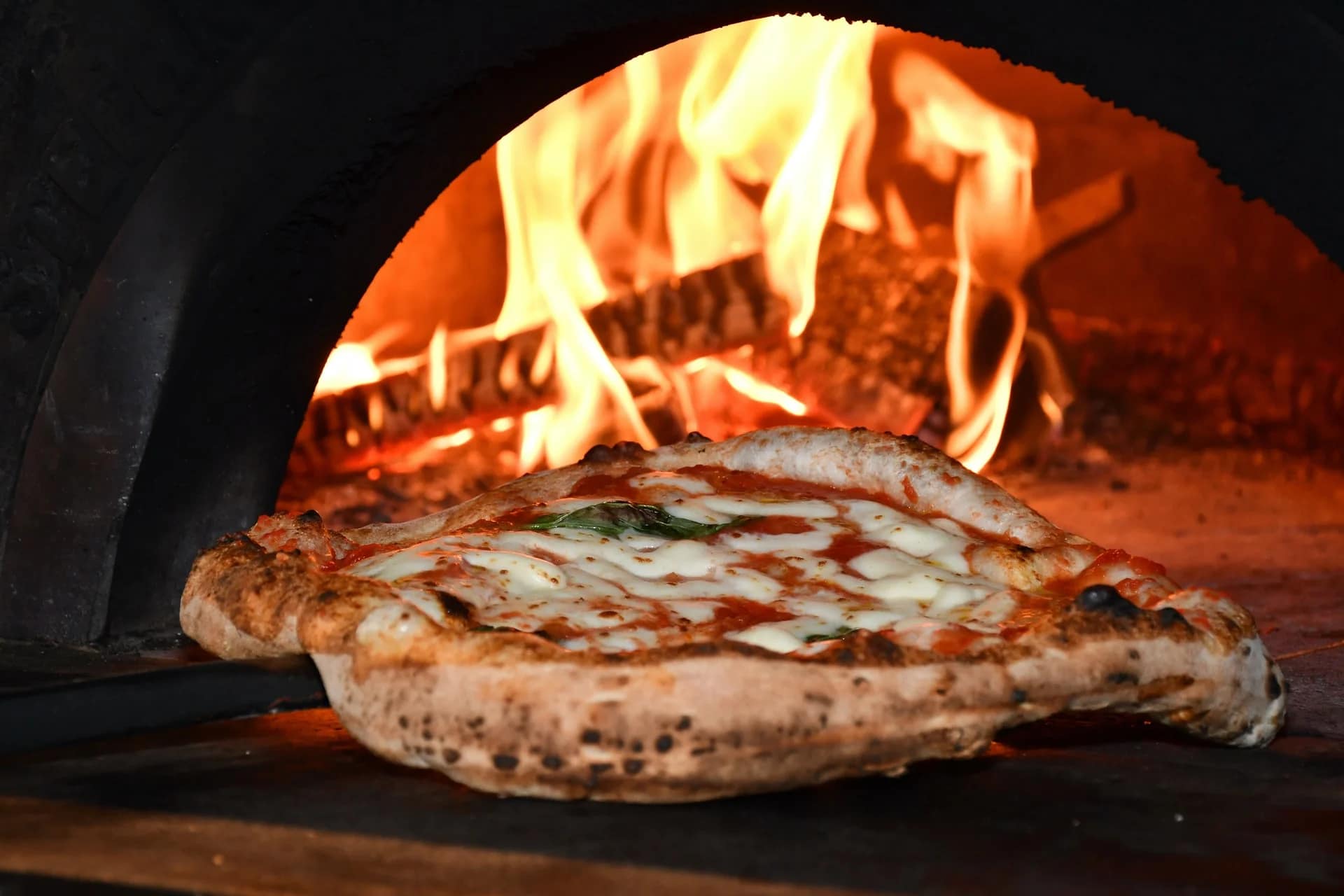 Une pizza Margherita fraîchement sortie du four à bois, avec des flammes ardentes en arrière-plan.