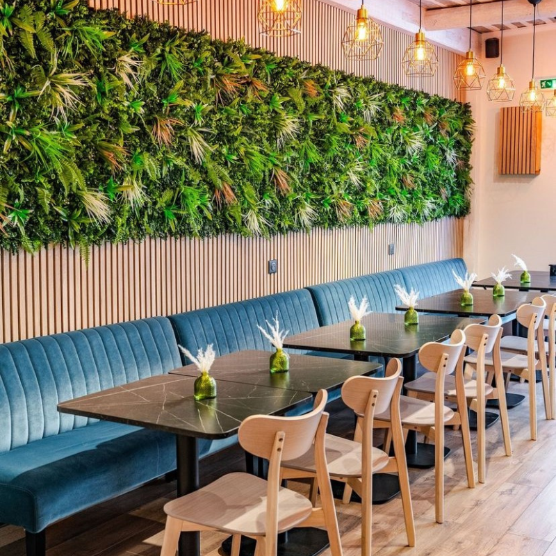 Un mur végétal luxuriant orne un restaurant avec des tables et banquettes modernes.