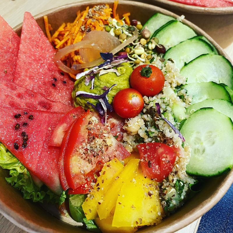 Un saladier rempli de pastèque, de quinoa, de concombres, de tomates cerises, d'avocat et de légumes râpés.