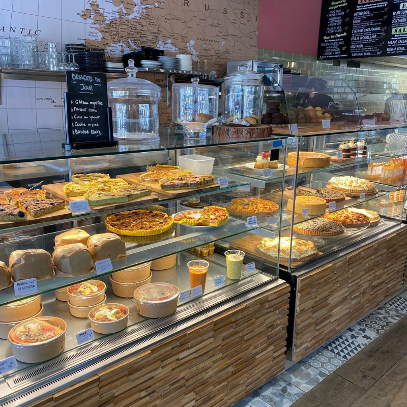 Une vitrine de boulangerie exposant des tartes, des quiches, des jus et des desserts dans des présentoirs en verre.