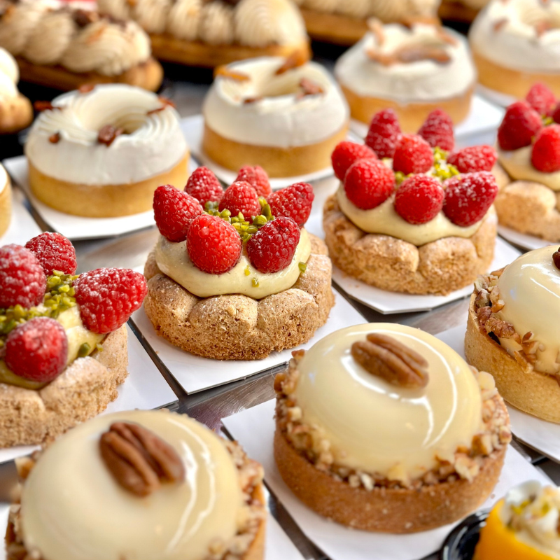Plusieurs petites pâtisseries, certaines garnies de framboises fraîches et de pistaches, d'autres de crème et de noix de pécan.