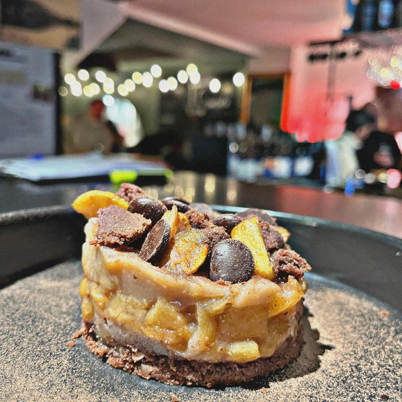 Une part de tarte aux fruits et chocolat sur une assiette sombre.