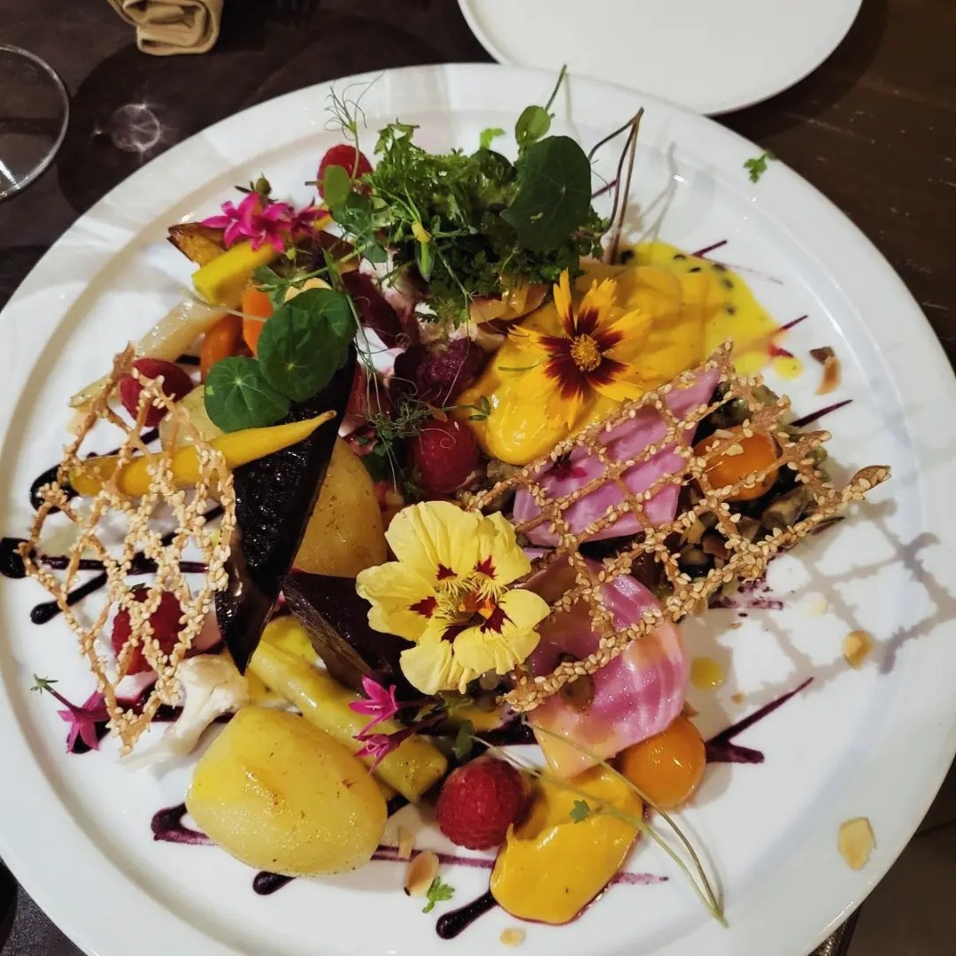 Une assiette blanche contenant une salade colorée de fruits et légumes, garnie de fleurs comestibles et de framboises.