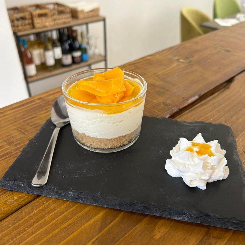 Un dessert à la mangue dans un verre, avec une boule de crème fouettée et une cuillère sur une ardoise, sur une table en bois.