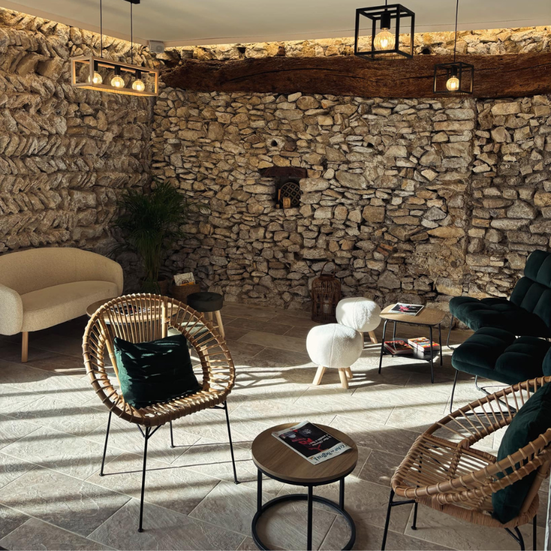 Une pièce avec des murs en pierre, un plafond en bois et des meubles modernes tels que des chaises en rotin et des canapés en velours.