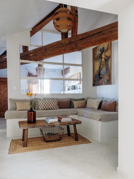 Un salon avec des poutres en bois apparentes, des fenêtres divisées, un canapé d'angle avec des coussins colorés, une table basse en bois et un tableau représentant un cheval.