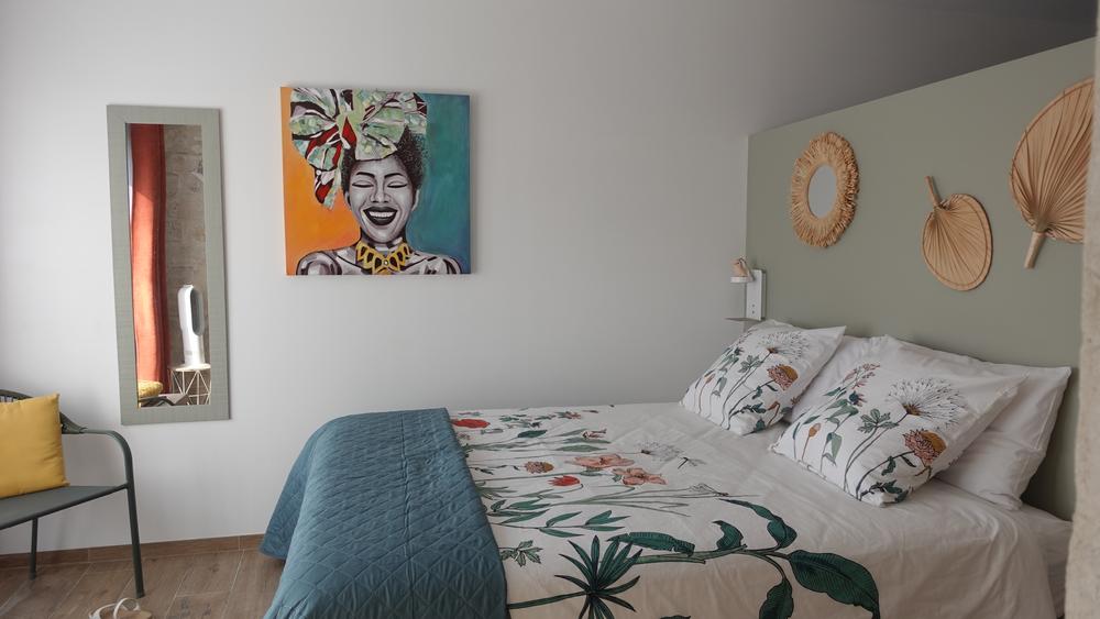 Une chambre avec un lit fleuri, une peinture murale colorée et des décorations murales en paille.
