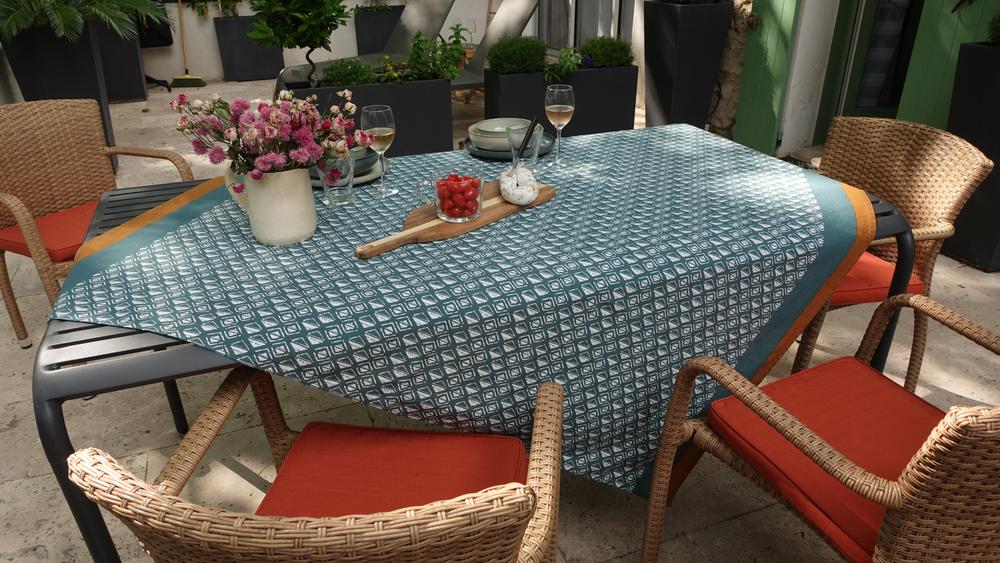 Une table de patio dressée avec une nappe à motifs, des verres de vin et des framboises fraîches, entourée de chaises en rotin.