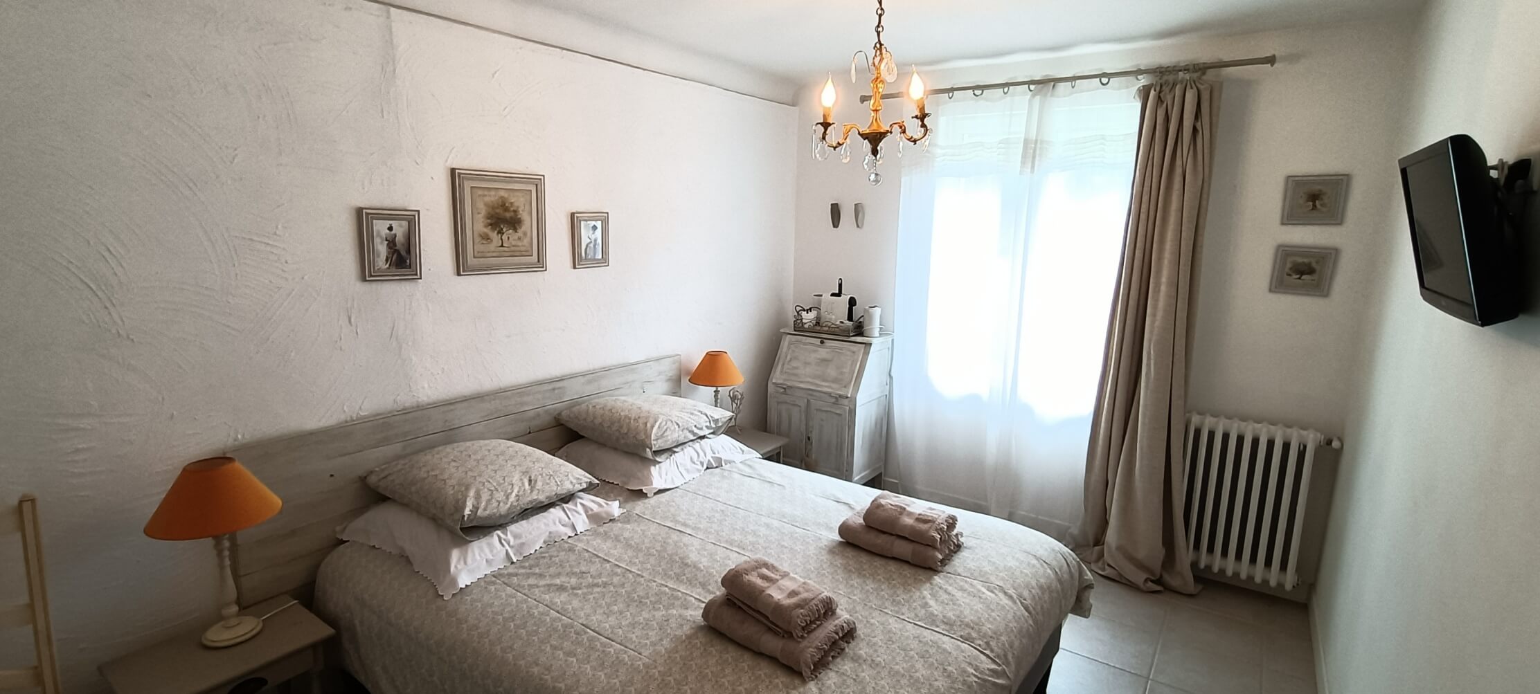 une chambre avec un lit double, le jour traversant les rideaux produit une ambiance tamisée