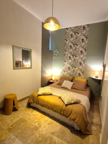 Une chambre moderne avec un lit double, une lampe suspendue dorée et du papier peint tropical.