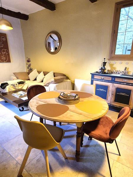 Une salle à manger chaleureuse avec une table ronde en bois, des chaises dépareillées et un canapé-lit en arrière-plan.