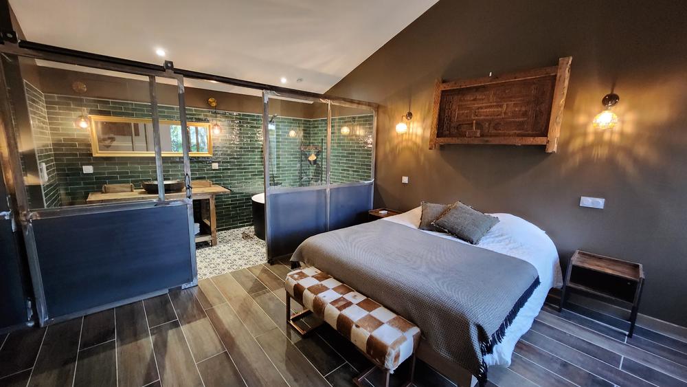 Une chambre moderne avec un lit double, une salle de bain ouverte avec une baignoire et des murs carrelés verts.