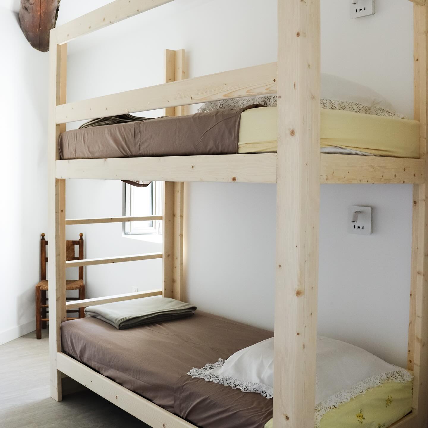 Un lit superposé en bois clair avec des matelas marron et des oreillers blancs dans une chambre lumineuse.