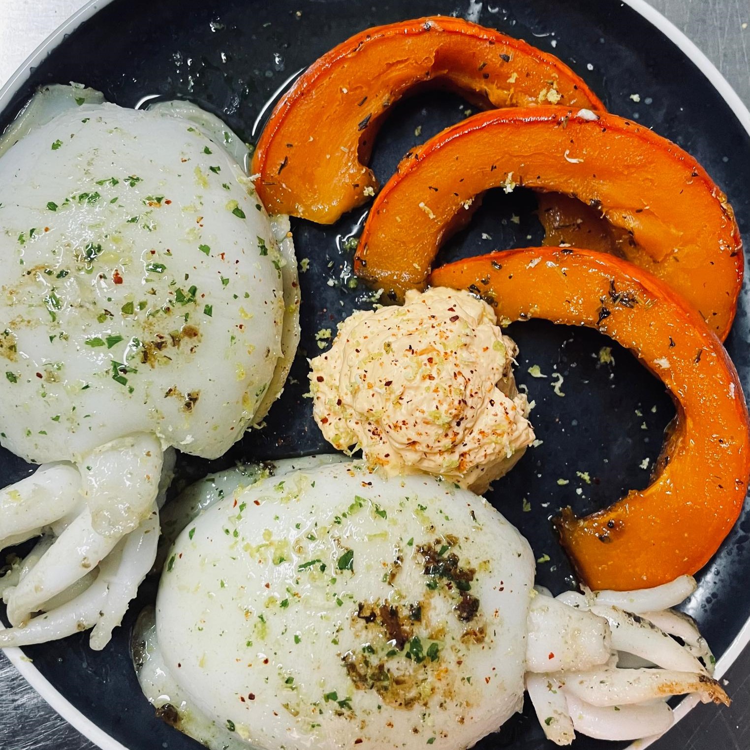 Un plat de fruits de mer grillés, composé de calamars et de tranches de courge rôtie.