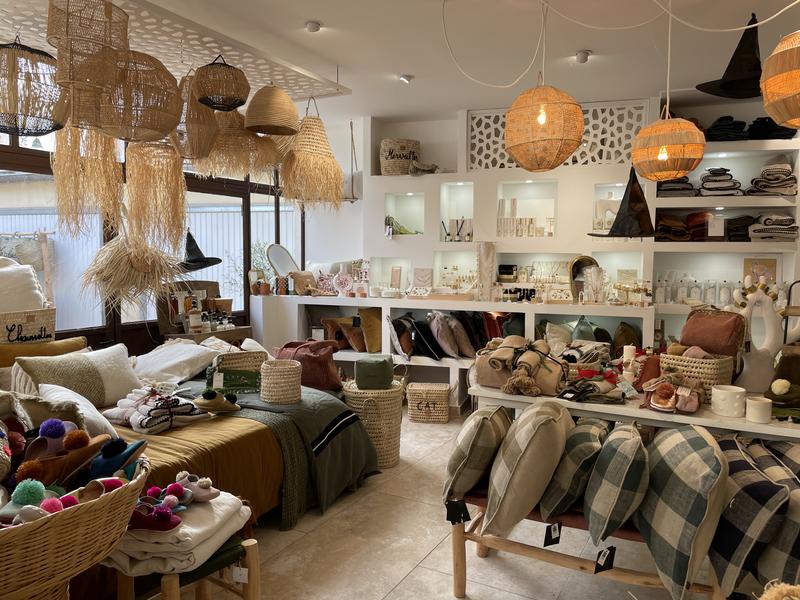 Cette vue intérieure met en avant une sélection d’objets de décoration et d’art de vivre : luminaires en fibres naturelles, coussins, linge de maison, paniers, accessoires et petits objets décoratifs. L’ensemble est présenté dans une atmosphère chaleureuse aux tons naturels.
